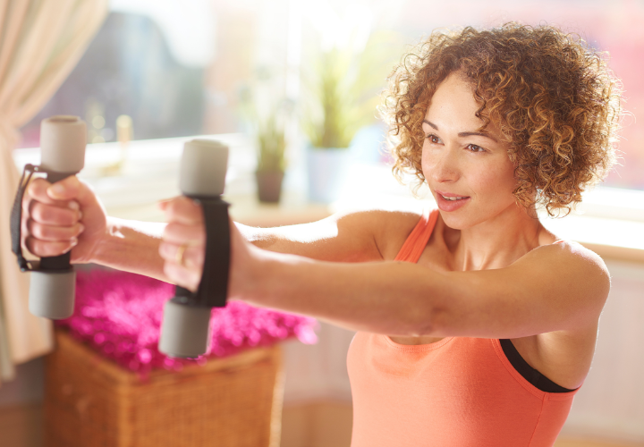 Woman performing a front raise exercise with light dumbbells during a home strength training workout.
