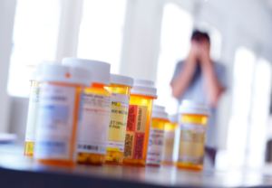 Prescription medication bottles in the foreground with a patient blurred in the background, representing polypharmacy and deprescribing.