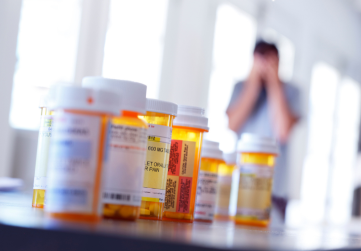 Prescription medication bottles in the foreground with a patient blurred in the background, representing polypharmacy and deprescribing.