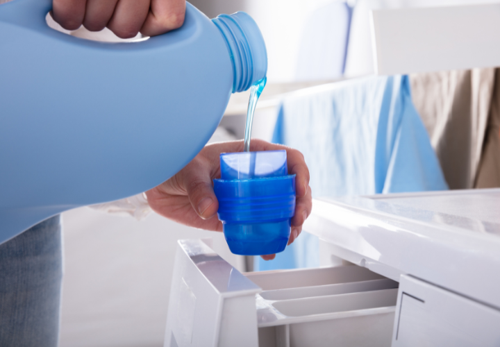 Person pouring liquid laundry detergent into a washing machine before starting a load of laundry.