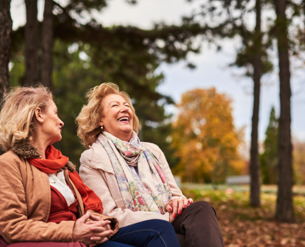 Two mature women laughing together outdoors, showing natural facial expression and emotional connection