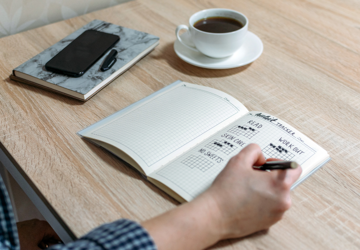 Person filling out a habit tracker to build consistent healthy habits